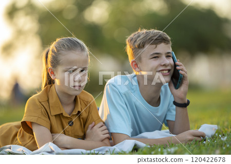 Happy young boy chatting on mobile phone ignoring his bored friend. Teenager friends having hard time communicating with each other. Friendship problems concept Happy young boy chatting on mobile phone ignoring his bored friend. Teenager friends having hard time communicating with each other. Friendship problems concept 120422678