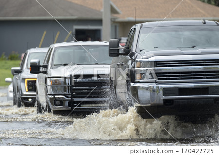 Flooded american street with moving vehicles surrounded with water in Florida residential area. Consequences of hurricane natural disaster Flooded american street with moving vehicles surrounded with water in Florida residential area. Consequences of hurricane natural disaster 120422725