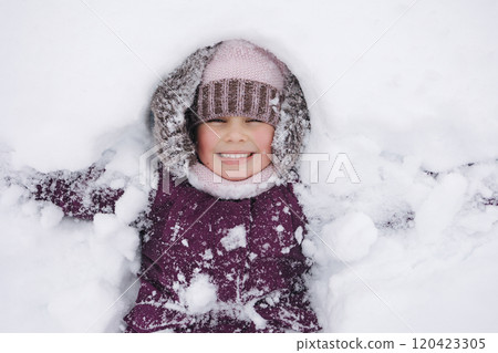 A little girl in winter clothing smiles joyfully while surrounded by deep snow, capturing the magic of a snowy winter day 120423305