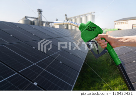 Hand with biofuel refueling nozzle on a background of solar panels and agricultural silos 120423421