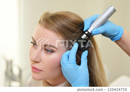 A dermatologist trichologist examines the hair structure of a young woman's patient using an optical dermatoscope device. 120424758