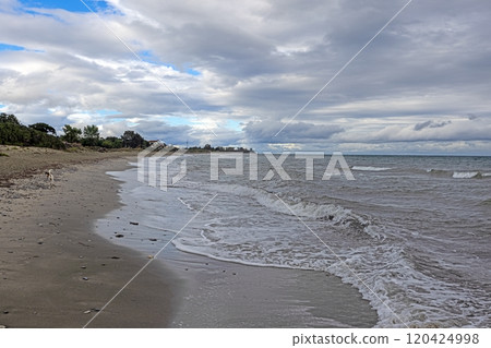 Gentle waves lapping on a vast sandy beach under a dynamic sky, offering a peaceful coastal vibe 120424998