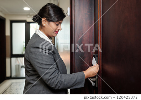 Smiling Woman Accessing Room with Key Card in Hallway 120425372
