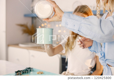 Family preparation of ginger biscuits with daughter. Focus on a little girl adding a flour. Woman wearing blue shirt and girl white t-shirt. Family preparation of ginger biscuits with daughter. Focus on a little girl adding a flour. Woman wearing blue shirt and girl white t-shirt. 120425800