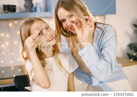 Blonde woman and her daughter holding a cookie cutters. Family preparation of ginger biscuits with child. Mother and daughter cooking cookies. Blonde woman and her daughter holding a cookie cutters. Family preparation of ginger biscuits with child. Mother and daughter cooking cookies. 120425802