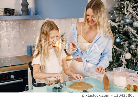 Family preparation of ginger biscuits with daughter. Mother and little girl cooking cookies. Blonde woman wearing blue shirt and girl white t-shirt. Family preparation of ginger biscuits with daughter. Mother and little girl cooking cookies. Blonde woman wearing blue shirt and girl white t-shirt. 120425803