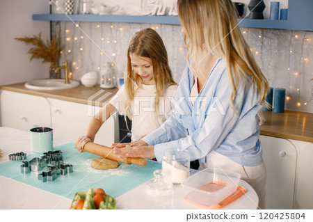 Family preparation of ginger biscuits with daughter. Mother and little girl cooking cookies. Blonde woman wearing blue shirt and girl white t-shirt. 120425804