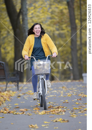 Happy middle aged woman rides a bicycle in the autumn park. Happy middle aged woman rides a bicycle in the autumn park. 120426833