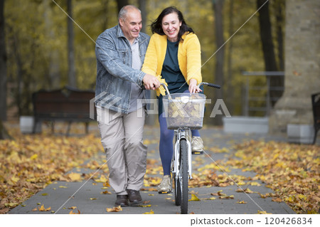 Happy middle aged couple with bike in autumn park. Elderly cheerful husband and wife on a walk. Happy middle aged couple with bike in autumn park. Elderly cheerful husband and wife on a walk. 120426834