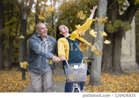 Happy middle aged couple with bike in autumn park. Elderly cheerful husband and wife on a walk. Happy middle aged couple with bike in autumn park. Elderly cheerful husband and wife on a walk. 120426835