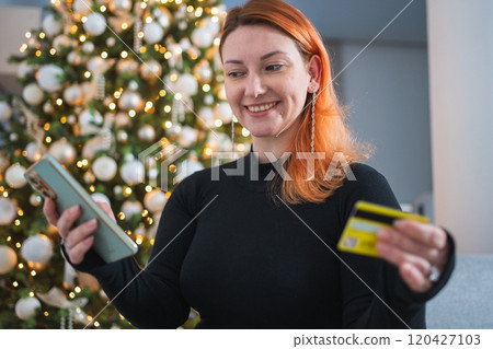 Christmas shopping. Woman shopping online holding smartphone paying with gold credit card for Christmas presents gifts. Girl buying on Internet enter credit card details. Christmas winter holidays 120427103