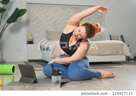 Yoga fitness workout training online. Woman practicing stretching with online app lessons at home. Plus size female doing sports exercise on yoga mat indoor. Girl have training workout for weight loss Yoga fitness workout training online. Woman practicing stretching with online app lessons at home. Plus size female doing sports exercise on yoga mat indoor. Girl have training workout for weight loss 120427115