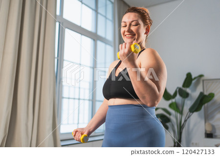 Fitness workout training. Woman picking up dumbbells. Plus size female doing sports exercise at home indoor. Girl in sportswear have workout weight training for weight loss. Sport and fitness 120427133