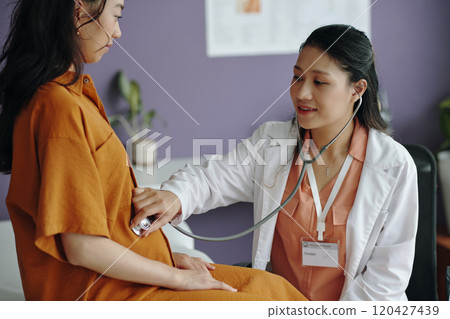 Doctor Examining Pregnant Patient with Stethoscope in Office 120427439
