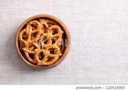 Salted pretzels in a wooden bowl on linen fabric, with empty space for text. Golden toasted small pretzels, in the traditional shape of a loop, made of wheat flour, used for snacking and dipping. 120428063