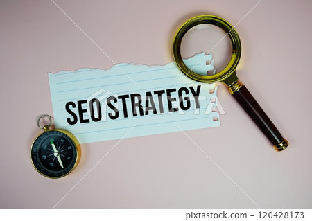 SEO Strategy text written on paper torn with compass and magnifying glass top view on pink background 120428173