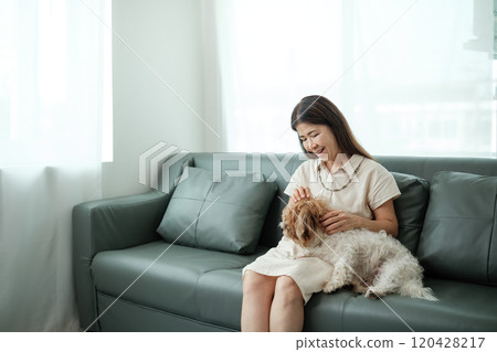 A woman is sitting on a couch with a white dog 120428217