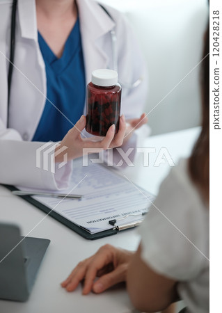 A doctor is holding a bottle of pills and talking to a patient 120428218