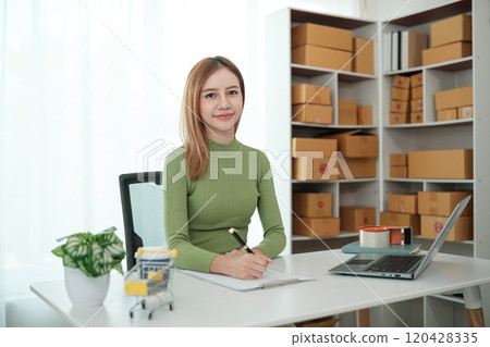 A woman is sitting at a desk with a laptop and a notebook 120428335