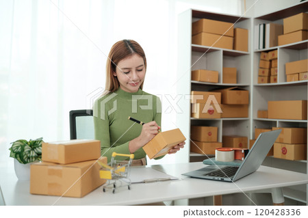 A woman is sitting at a desk with a laptop and a stack of boxes 120428336