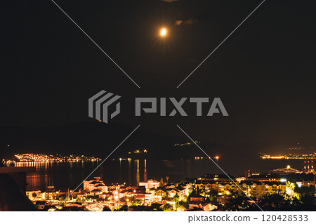 A tranquil night over the coastal town with a glowing moon reflecting on calm waters 120428533