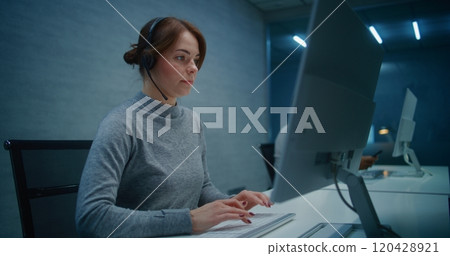 Call center office at night: Female technical support specialist in headset monitors data on PC 120428921