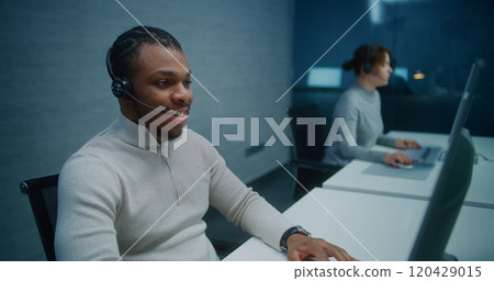 African American helpdesk specialist talks on headset with customer, works on computer 120429015