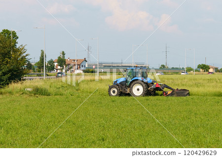 Tractor mows green grass on a summer day. Tractor mows green grass on a summer day. 120429629