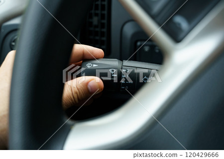 A man's hand turns on the windshield wiper switch control lever in a truck 120429666