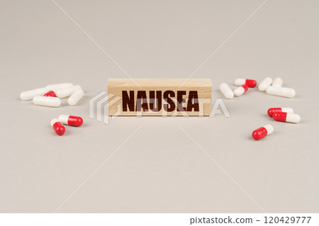 On a gray surface are tablets, capsules and a wooden plate with the inscription - Nausea On a gray surface are tablets, capsules and a wooden plate with the inscription - Nausea 120429777