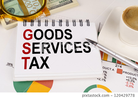 On the table is a cup of coffee, money, business charts and a notepad with the inscription - GOODS SERVICES TAX 120429778