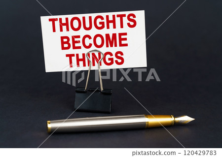 On the black surface is a pen, an office paper clip with a business card on which is written - Thoughts Become Things 120429783