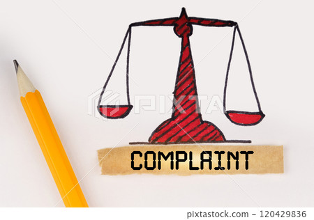Next to the painted scales of justice lies a pencil and a strip of paper with the inscription - Complaint Next to the painted scales of justice lies a pencil and a strip of paper with the inscription - Complaint 120429836
