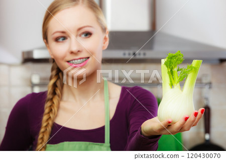 Woman in kitchen holds raw fennel bulb vegetable 120430070