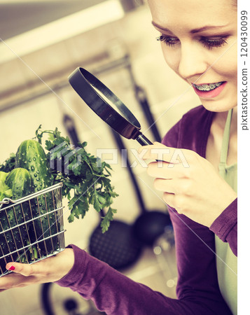 Woman looking through magnifier at vegetables basket 120430099