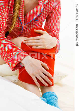 Woman holding warm red hot water bottle 120430357