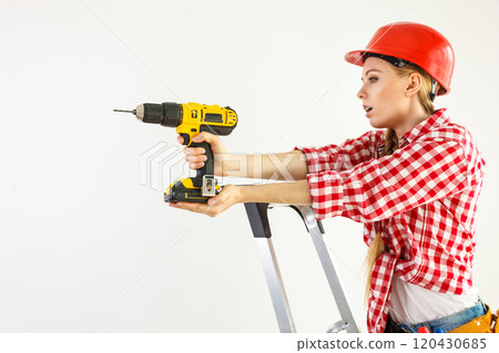 Woman using drill on ladder 120430685