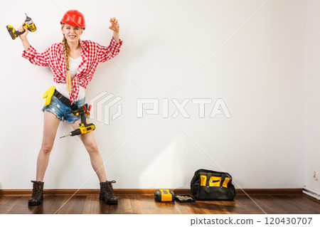 Woman wearing helmet, toolbelt about to drill wall Woman wearing helmet, toolbelt about to drill wall 120430707