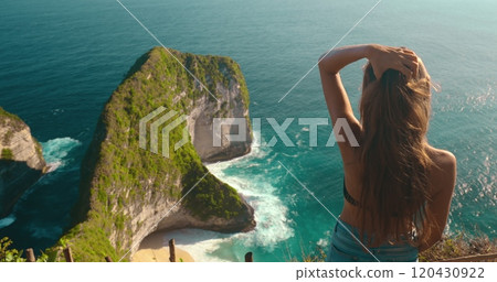 Young tourist woman is touching her hair while enjoying the view from a cliff on kelingking secret point beach in nusa penida, bali Young tourist woman is touching her hair while enjoying the view from a cliff on kelingking secret point beach in nusa penida, bali 120430922