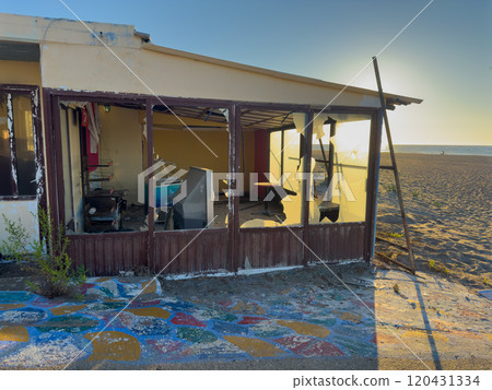 Abandoned Beachside Structure With Broken Windows Illuminated by Sunset Glow Near Sandy Shore 120431334