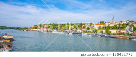 The serene waters of the Sava River flow through Belgrade, Serbia, surrounded by lush greenery and historic buildings under a clear blue sky. Boats line the riverbank, inviting exploration. The serene waters of the Sava River flow through Belgrade, Serbia, surrounded by lush greenery and historic buildings under a clear blue sky. Boats line the riverbank, inviting exploration. 120431772