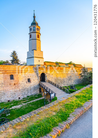 The Clock Tower stands majestically at Kalemegdan Fortress during sunset. The soft orange glow highlights the ancient stone walls and the serene landscape surrounding this historic site. The Clock Tower stands majestically at Kalemegdan Fortress during sunset. The soft orange glow highlights the ancient stone walls and the serene landscape surrounding this historic site. 120431776