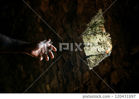 Hand reaches into a hole in the brickwork through which light is visible Hand reaches into a hole in the brickwork through which light is visible 120431897