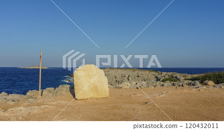 A solitary limestone rock stands against a serene coastal backdrop under a clear blue sky. 120432011