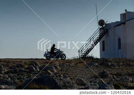 Riding into serenity: A lone motorcyclist approaches a remote building at dusk. 120432016