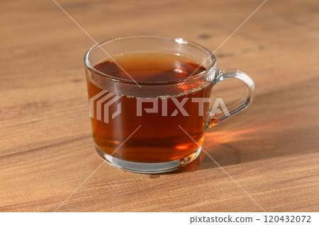 A cozy glass of freshly brewed tea resting on a wooden table in the warm afternoon sunlight 120432072