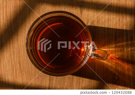 Warm cup of tea rests on a wooden table, basking in soft afternoon sunlight 120432086