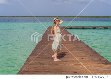 Female tourist in a turquoise dress standing on a wooden pier over the turquoise waters of Bacalar Lake, Mexico. Peaceful tropical travel destination concept Female tourist in a turquoise dress standing on a wooden pier over the turquoise waters of Bacalar Lake, Mexico. Peaceful tropical travel destination concept 120432706