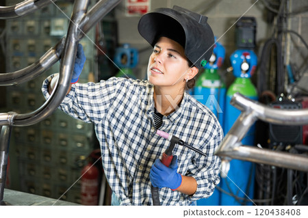 Portrait of a female welder standing with a welding machine and a safety helmet in metal machining workshop Portrait of a female welder standing with a welding machine and a safety helmet in metal machining workshop 120438408