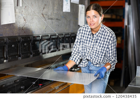 Female worker operating metal press brake in workshop 120438435